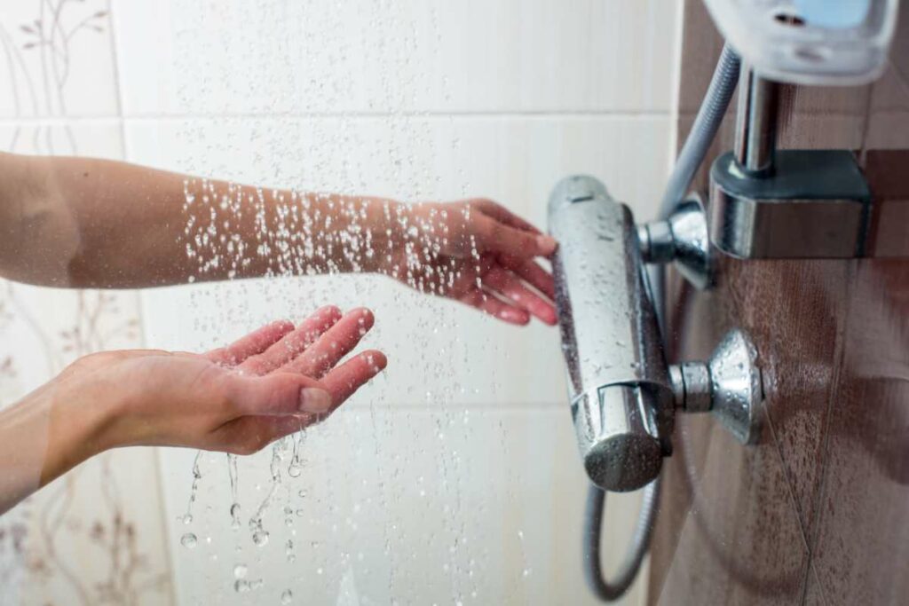 Hands testing the temperature in a shower.